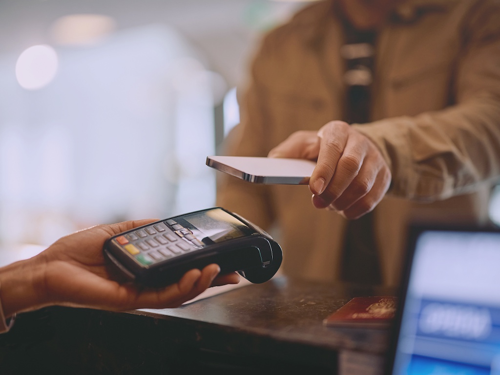Contactless payment being made via a smartphone on a POS terminal, symbolizing secure, remote networking for retail and financial transactions.
